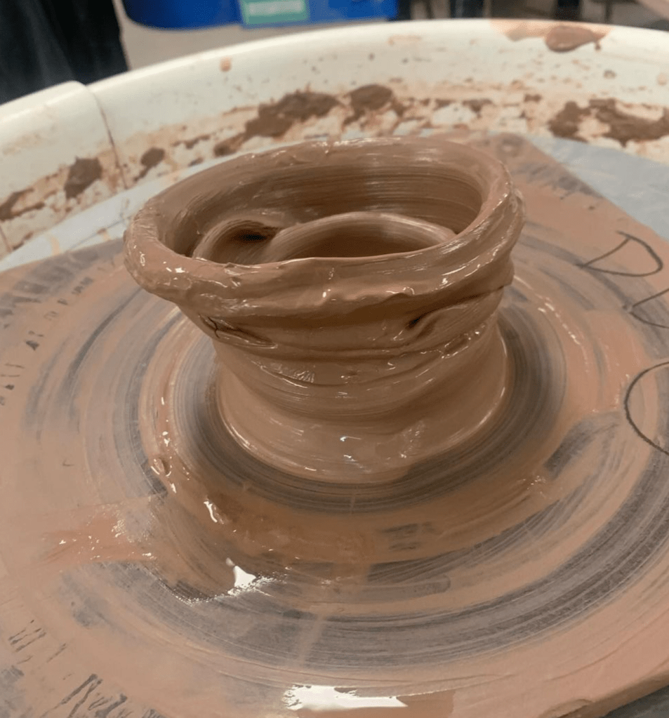 close up of clay on the wheel. the clay is in the shape of a collapsed vase.